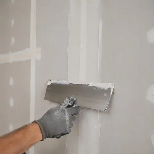 Taping knife spreading joint compound along a seam, working wide to keep the joint flat