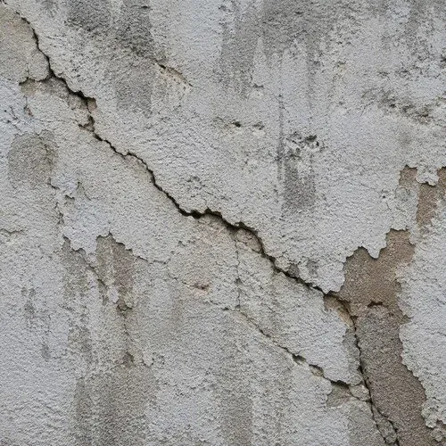 Cracked exterior stucco wall with a chipped, spalling surface letting water behind it
